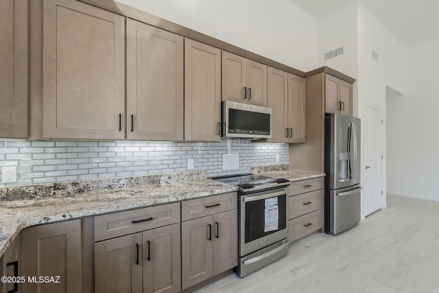 kitchen featuring visible vents, backsplash, appliances with stainless steel finishes, and light stone countertops