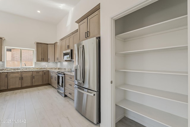 kitchen with light stone counters, open shelves, a sink, appliances with stainless steel finishes, and decorative backsplash