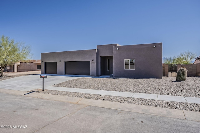 pueblo-style house featuring concrete driveway, fence, a garage, and stucco siding