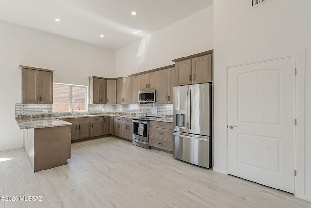 kitchen with backsplash, light stone countertops, a peninsula, a high ceiling, and stainless steel appliances