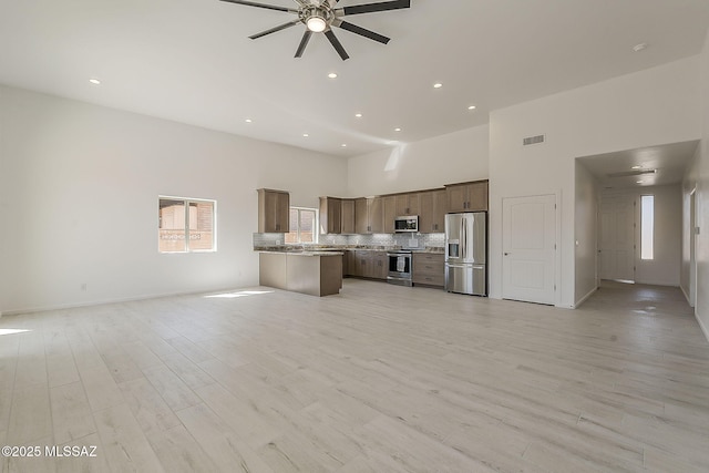 unfurnished living room with visible vents, ceiling fan, recessed lighting, light wood-style flooring, and a towering ceiling