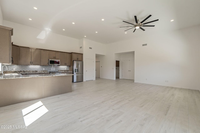 kitchen featuring backsplash, open floor plan, a peninsula, light wood-style floors, and stainless steel appliances