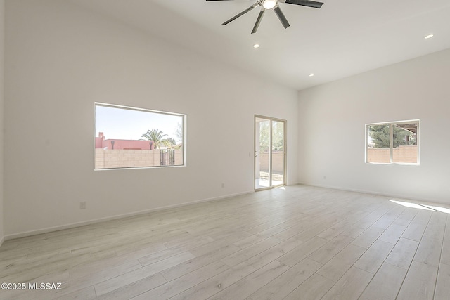 spare room with baseboards, light wood-type flooring, a high ceiling, and a ceiling fan