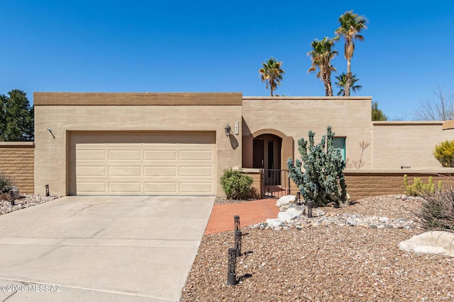 pueblo-style house with a garage, driveway, and stucco siding