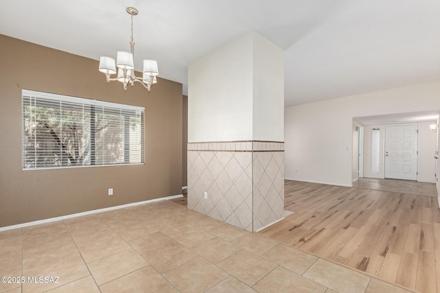 spare room with a chandelier, light tile patterned floors, and wainscoting