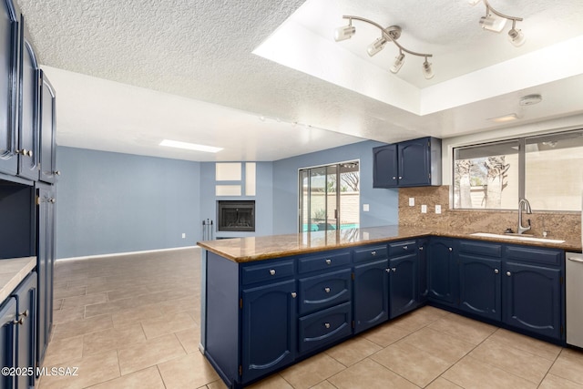 kitchen featuring a peninsula, a fireplace, a sink, blue cabinets, and tasteful backsplash