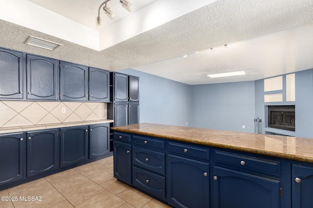 kitchen with decorative backsplash, blue cabinetry, light tile patterned flooring, and a textured ceiling