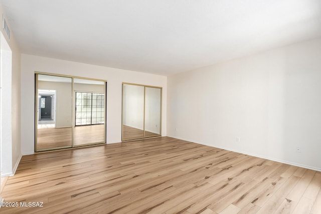 unfurnished bedroom featuring two closets and light wood-style floors