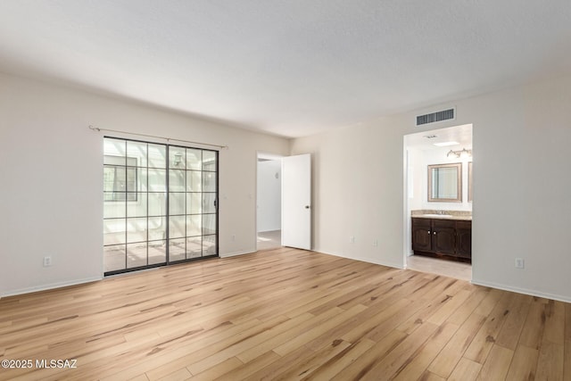 unfurnished bedroom featuring visible vents, connected bathroom, baseboards, light wood-style flooring, and a sink