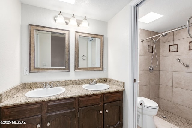 full bath featuring double vanity, a tile shower, toilet, and a sink