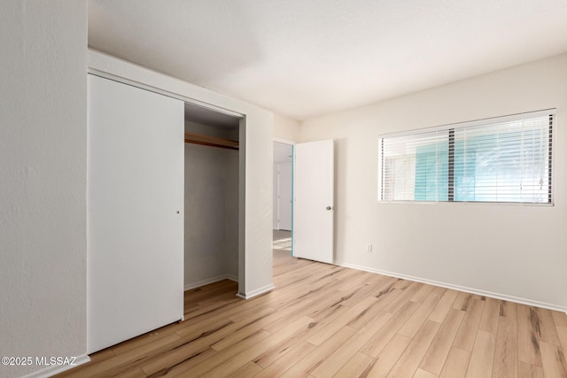 unfurnished bedroom featuring baseboards, light wood-type flooring, and a closet