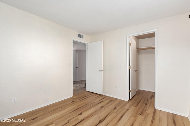 unfurnished bedroom featuring light wood-type flooring, visible vents, baseboards, and a spacious closet