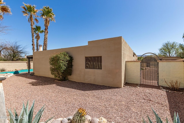 view of side of property with a gate, fence, and stucco siding