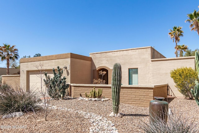 pueblo-style home featuring stucco siding, a garage, and fence