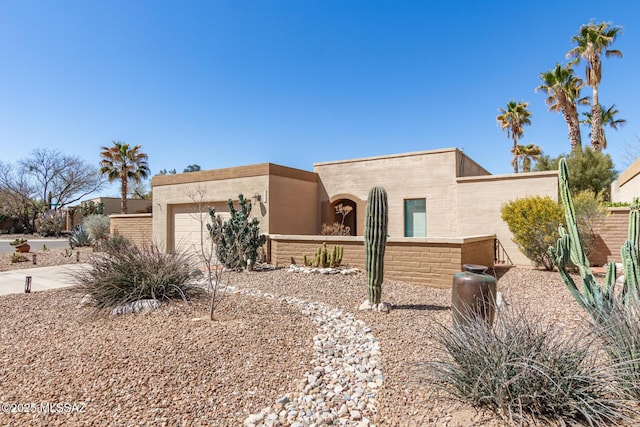 pueblo-style home with stucco siding, an attached garage, and fence