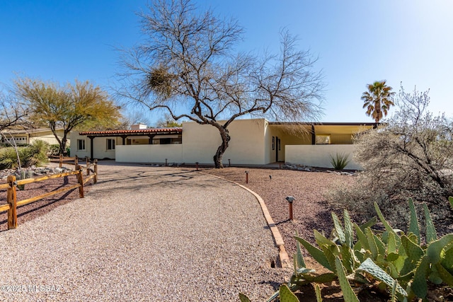 view of front of home featuring stucco siding, gravel driveway, and fence