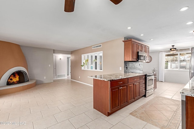 kitchen featuring light stone counters, light tile patterned floors, ceiling fan, stainless steel appliances, and a large fireplace