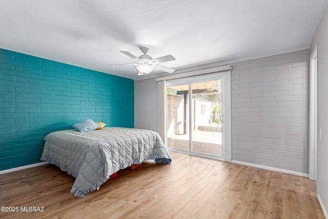 bedroom with a ceiling fan, wood finished floors, baseboards, brick wall, and access to exterior