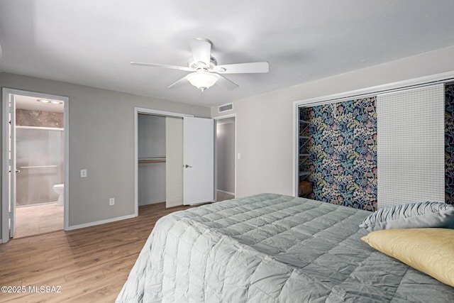 bedroom with wood finished floors, visible vents, baseboards, ensuite bath, and ceiling fan