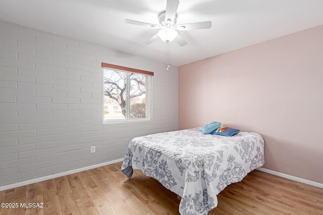 bedroom with ceiling fan, baseboards, wood finished floors, and brick wall