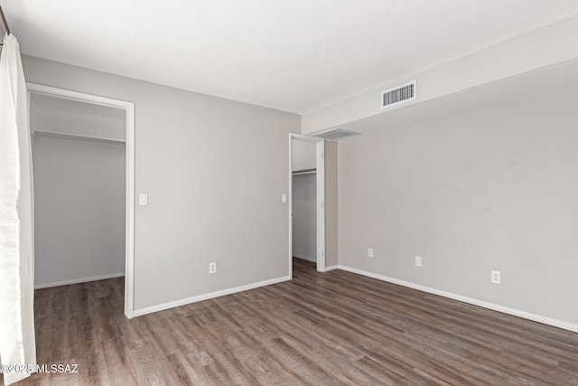 unfurnished bedroom with a walk in closet, wood finished floors, visible vents, and baseboards