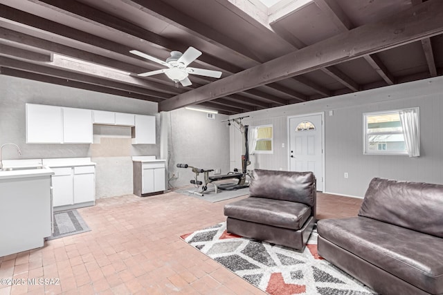 living room with brick floor, beam ceiling, and a ceiling fan