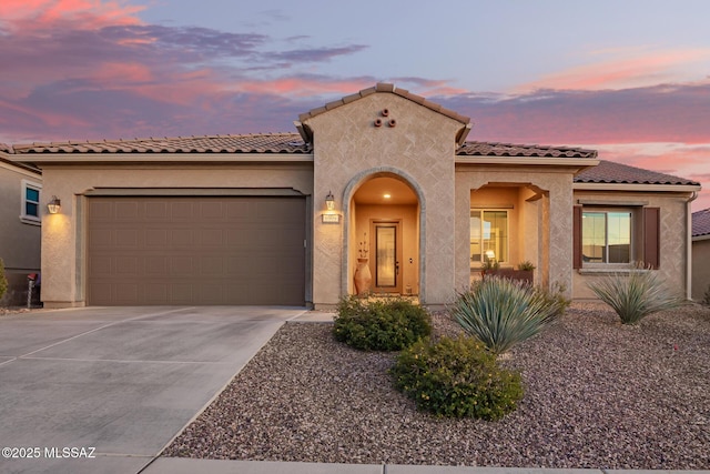 mediterranean / spanish-style house with stucco siding, driveway, a tile roof, and a garage