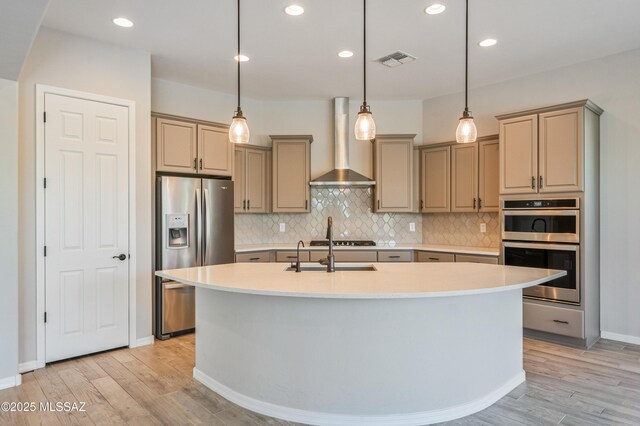 6909 W Cliff Spring Trl, Marana, AZ 85658 - kitchen with appliances with stainless steel finishes, wall chimney range hood, light wood-type flooring, light countertops, and tasteful backsplash