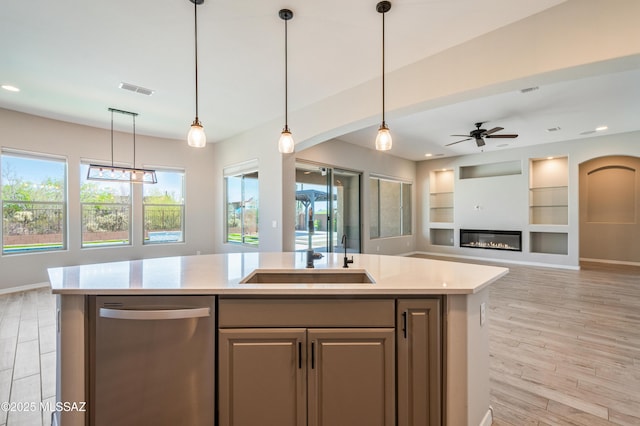 6909 W Cliff Spring Trl, Marana, AZ 85658 - kitchen with dishwasher, open floor plan, an island with sink, hanging light fixtures, and a glass covered fireplace