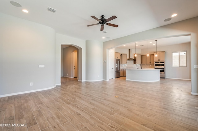 6909 W Cliff Spring Trl, Marana, AZ 85658 - unfurnished living room with arched walkways, a ceiling fan, light wood-type flooring, recessed lighting, and baseboards