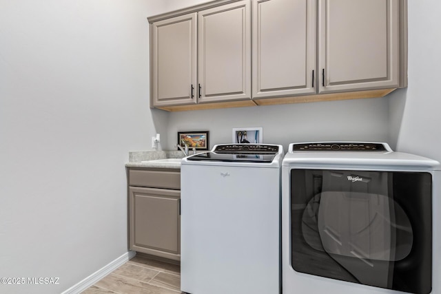 laundry room with light wood-style flooring, a sink, washing machine and dryer, cabinet space, and baseboards