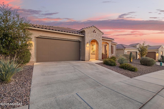 mediterranean / spanish house featuring stucco siding, concrete driveway, an attached garage, and a tile roof