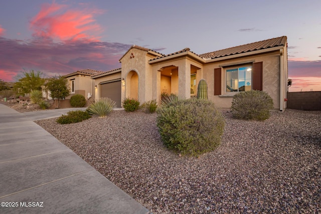 mediterranean / spanish-style home featuring a tiled roof, a garage, driveway, and stucco siding