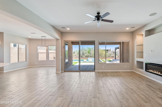 6909 W Cliff Spring Trl, Marana, AZ 85658 - unfurnished living room featuring light wood-style floors, built in features, baseboards, a glass covered fireplace, and recessed lighting