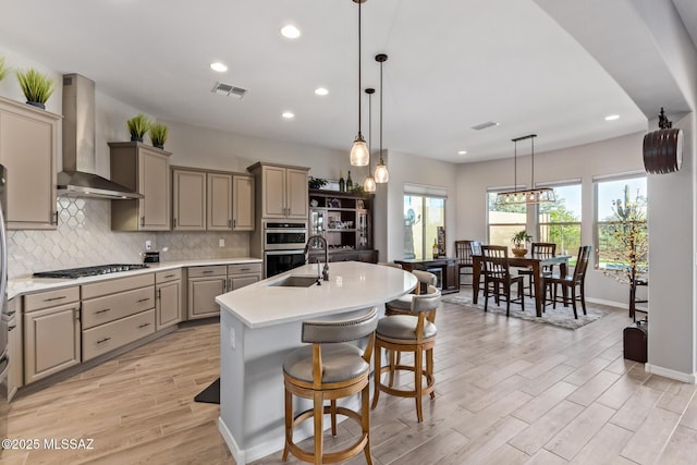 kitchen with light countertops, wall chimney exhaust hood, visible vents, and a sink