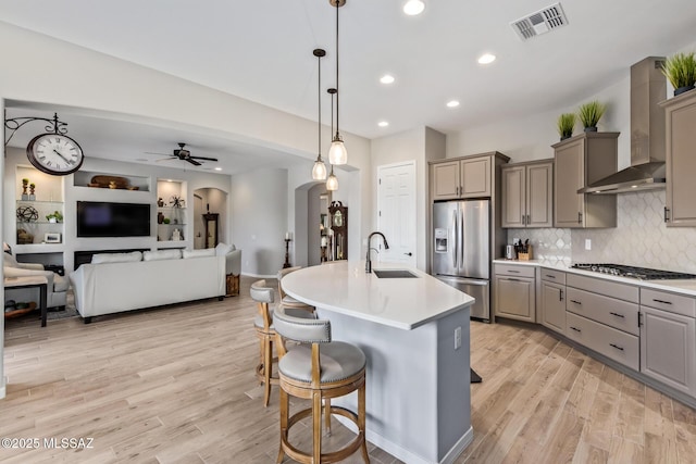 kitchen featuring arched walkways, a sink, gray cabinetry, appliances with stainless steel finishes, and wall chimney exhaust hood