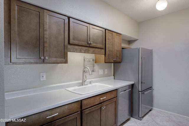 kitchen featuring baseboards, a sink, dark brown cabinetry, light countertops, and appliances with stainless steel finishes