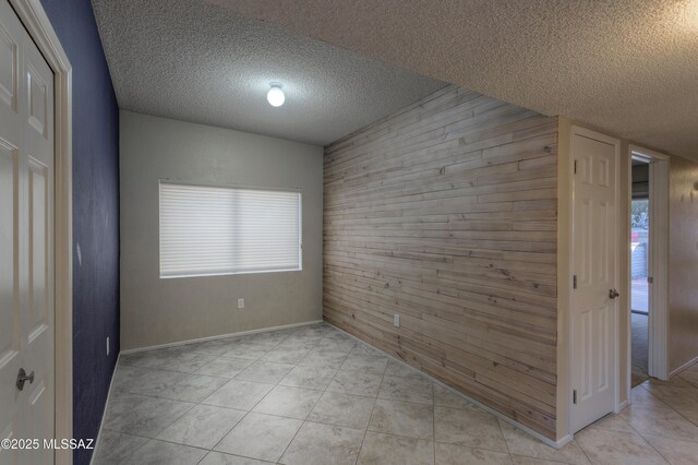 empty room with wooden walls, light tile patterned floors, and a textured ceiling