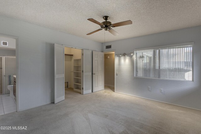 unfurnished bedroom featuring visible vents, a textured ceiling, connected bathroom, and light colored carpet