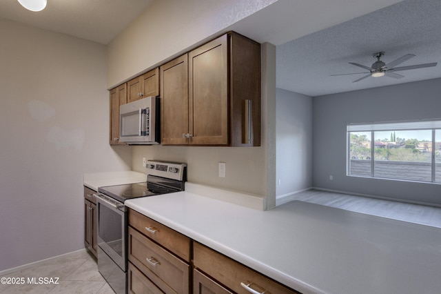 kitchen with open floor plan, light countertops, light tile patterned floors, stainless steel appliances, and a ceiling fan