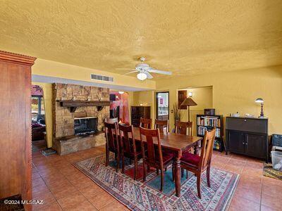 dining area with tile patterned floors, visible vents, a stone fireplace, and a ceiling fan