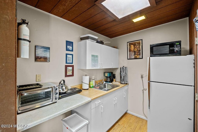 kitchen with freestanding refrigerator, a sink, black microwave, white cabinetry, and wooden ceiling