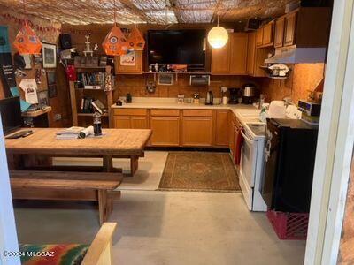 kitchen with white range with electric stovetop, wall chimney exhaust hood, light countertops, and concrete flooring