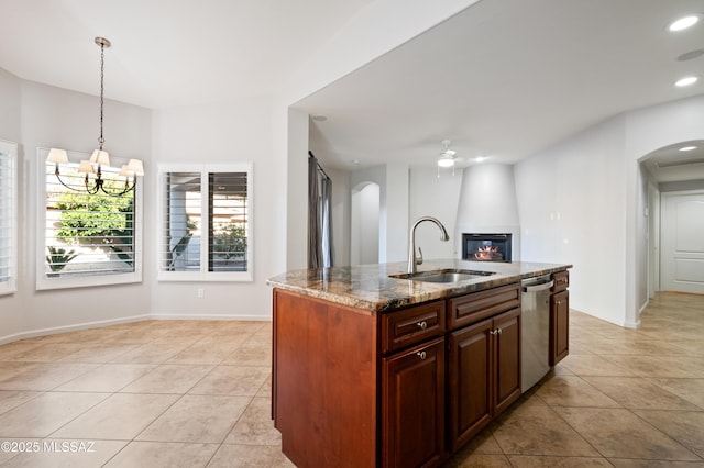 kitchen featuring light stone counters, arched walkways, a sink, dishwasher, and a large fireplace