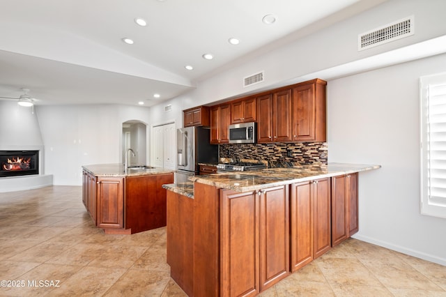 kitchen with visible vents, stone countertops, a sink, stainless steel appliances, and ceiling fan