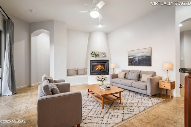 living room with arched walkways, light tile patterned floors, a large fireplace, and a ceiling fan