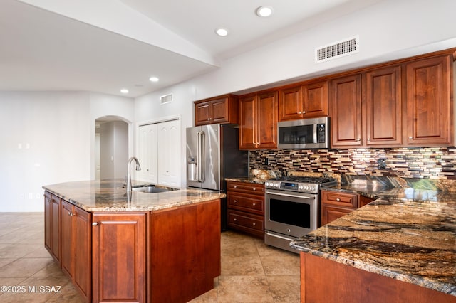 kitchen with decorative backsplash, appliances with stainless steel finishes, dark stone counters, and a sink