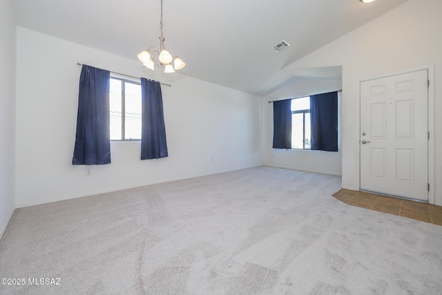 carpeted spare room featuring an inviting chandelier, visible vents, and vaulted ceiling