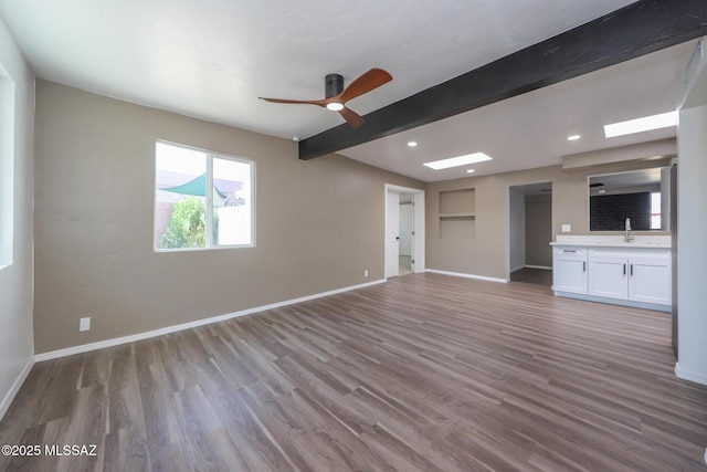 unfurnished living room with a sink, beamed ceiling, baseboards, and wood finished floors