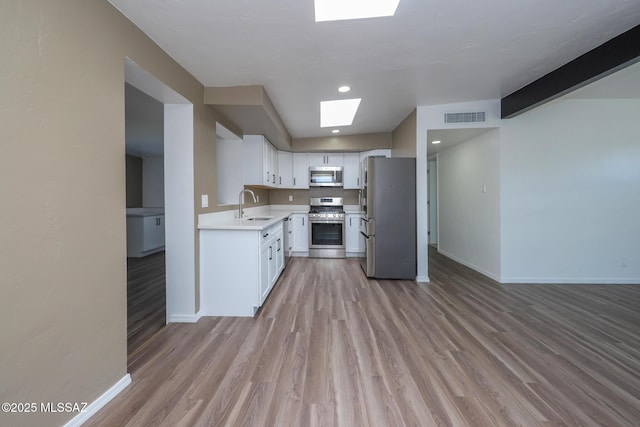 kitchen with visible vents, a sink, stainless steel appliances, light countertops, and light wood-type flooring